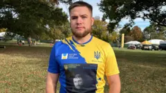 Dmytro Kamenschyk com camiseta azul e amarela, cores da bandeira da Ucrânia, e a foto do pai dele em preto e branco