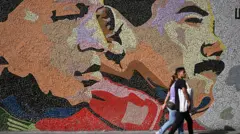 Um casal caminha diante de um mural com os rostos de Hugo Chávez e Nicolás Maduro