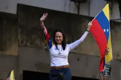 María Corina Machado sorrindo e erguendo os braços e bandeira da Venezuela em protesto