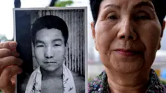 Hideko Hakamata (91) u košulji cvetnog dezena sa kratkom kosom drži u ruci crno belu fotografiju brata i gleda u kameru