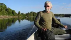 Idoso de cabelo branco em barco em rio caudaloso