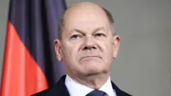 Foto do chanceler alemão Olaf Scholz, inexpressivo em frente a uma bandeira vermelha e preta