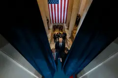 Foto tirada do alto mostra Trump e comitiva caminhando em direção a porta, com bandeira dos EUA ao fundo