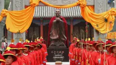 Estátua de Confúcio em comemoração, várias pessoas amarelas vestidas de vermelho em volta