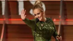 Adele acena com a estatueta do Grammy em uma das mãos