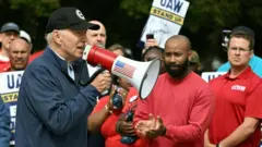 Biden discursando com megafone vermelho em piquete