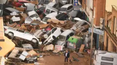 Idoso e cachorro em frente a carros amontoados arrastados pela chuva