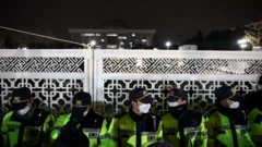 한국 대통령이 계엄령을 선포한 후, 모자와 마스크, 형광 조끼를 착용한 경찰들이 국회 정문 앞을 지키고 있다.