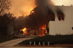 Mansão pegando foco, com letreiro dizendo 'paz' em frente à casa intacto