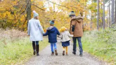 Família de costas andando de mãos dadas em parque