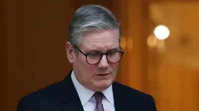 Sir Keir Starmer wearing dark suit and glasses looks down at floor