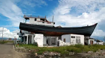 Endonezya'nın Açe bölgesinde yıkılmış bir binanın üzerinde, felaketten neredeyse bir yıl sonra hala duran balıkçı teknesi.