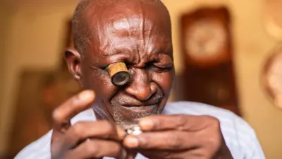 A close-up of Bala Muhammad looking at a watch through a special eye-glass in his right eye