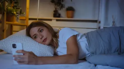 Woman lies in bed at night looking at her smartphone