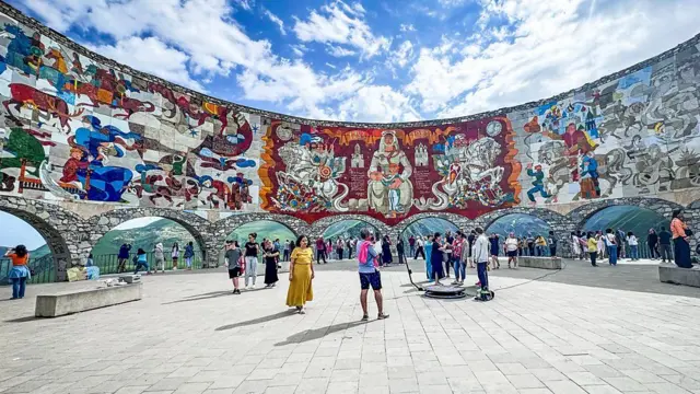 Monumento à Amizade Rússia-Geórgia com pinturas coloridas e pessoas abaixo tirando fotos da paisagem montanhosa