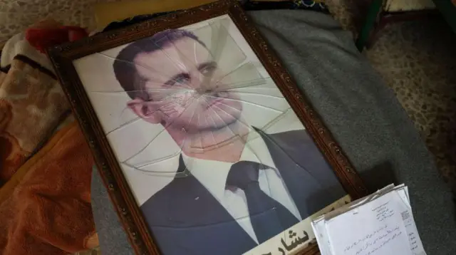 Um porta-retrato quebrado com a foto de Bashar al-Assad caído no chão