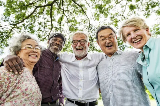 Cinco idosos se abraçam e sorriem