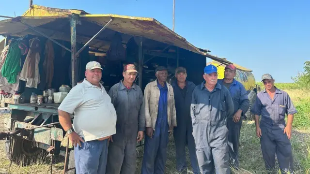 Sete homens posando para foto em frente a alojamento improvisado