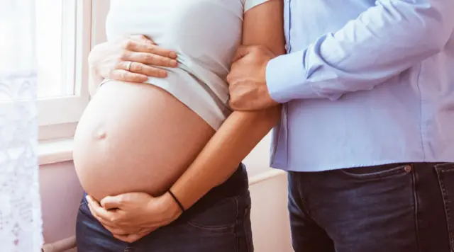 Barriga de uma mulher branca grávida com mão masculina branca segurando seu braço