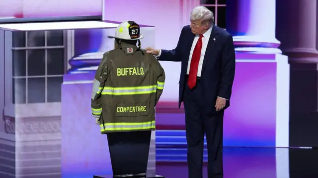 Republican presidential nominee and former U.S. President Donald Trump touches the turnout coat and helmet of former Buffalo Township Volunteer Fire Department chief Corey Comperatore, who was killed at his rally last week, as he gives his acceptance speech on Day 4 of the Republican National Convention (RNC), at the Fiserv Forum in Milwaukee, Wisconsin, U.S., July 18, 2024.