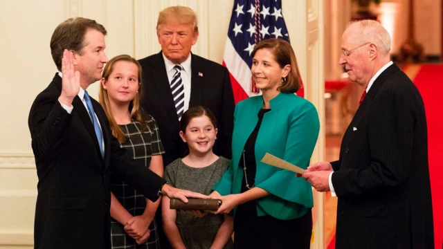 Juiz Brett Kavanaugh fazendo juramento durante posse, observado por família e Trump