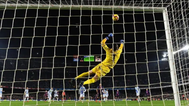 Goleiro salta para pegar bola em partida em estádio de futebol