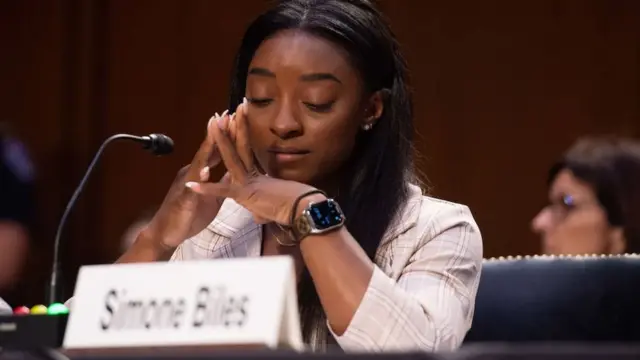 Simone Biles de olhos fechados e com as mão juntas em depoimento