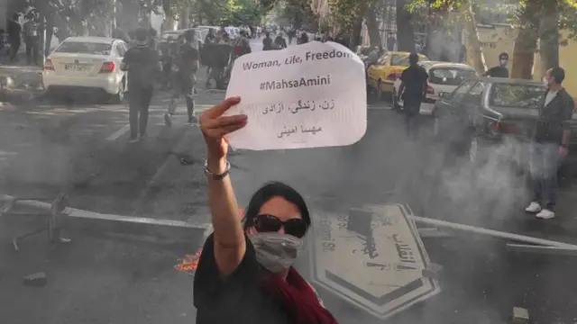 Uma mulher iraniana com a cabeça descoberta mostra uma placa com o slogan "mulher, vida, liberdade" durante um protesto