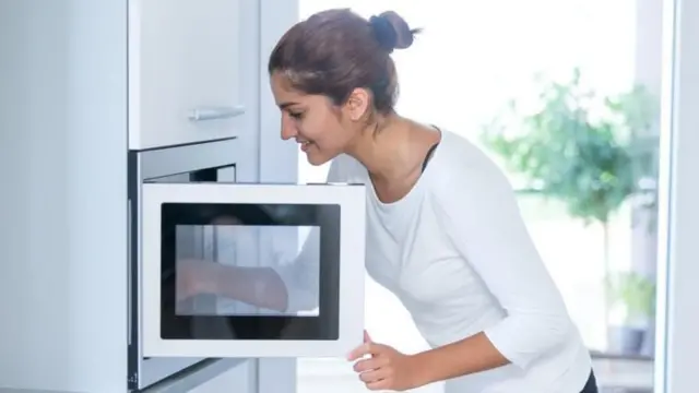 Mulher abrindo a porta do micro-ondas