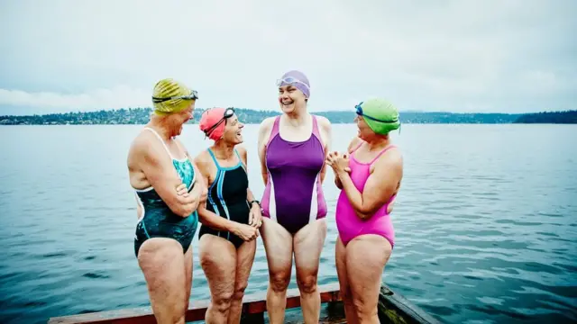 Quatro mulheres de meia-idade sorridentes de maiô em frente a um lago