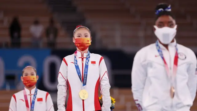 A medalhista de ouro Chenchen Guan da Team China observa durante a cerimônia de medalha final da trave de equilíbrio de ginástica feminina com a atleta norte-americana Simone Biles à sua esquerda