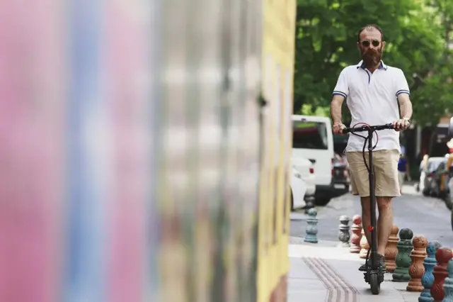 Homem pilotando um patinete elétrico em uma calçada