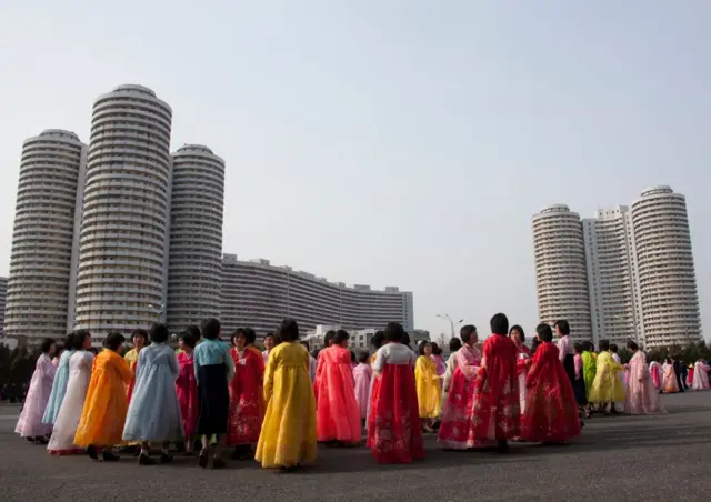 Mulheres vestidas com trajes tradicionais em frente a blocos de apartamentos