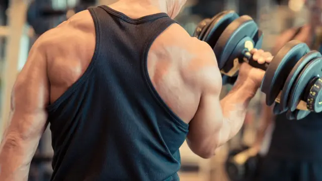 Homem musculoso de costas na academia, erguendo halter com um dos braços