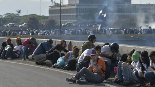 Pessoas agachadas na rua em Caracas em meio a confronto