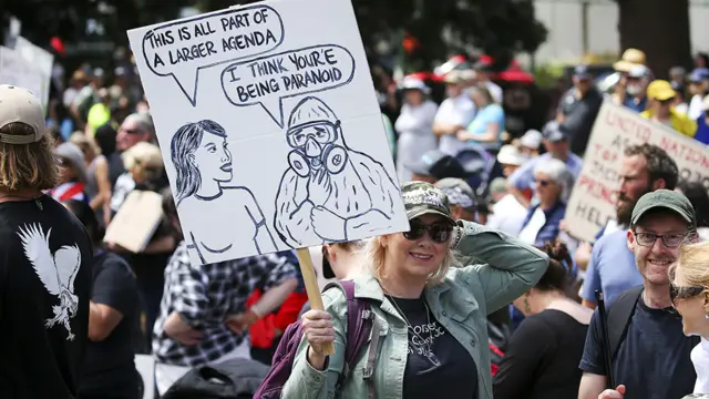 Manifestante segura cartaz com dizeres em inglês "é tudo parte da propaganda liberal"