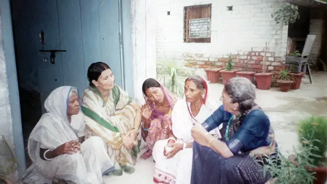 Anila, de sari verde, branco e dourado, conversando com um grupo de parteiras — todas sentadas no chão. Foto de arquivo da década de 1990.