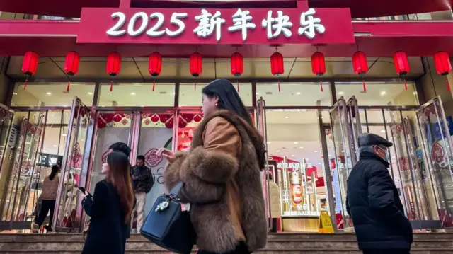 Pedestres passam por um shopping decorado com lanternas vermelhas e uma placa com os dizeres "Feliz Ano Novo 2025" para celebrar o próximo Ano Novo Chinês em 14 de janeiro de 2025 em Chongqing, China