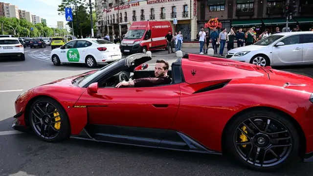 Tristan Tate dirigindo um carro esportivo vermelho em Bucareste, 2024