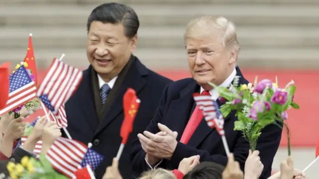 O presidente dos EUA, Donald Trump, um homem branco idoso à direita, e Xi Jinping, presidente da China, um homem amarelo e idoso, cumprimentam pessoas que agitam bandeiras nacionais americanas e chinesas durante uma cerimônia de boas-vindas do lado de fora do Grande Salão do Povo em Pequim, China, na quinta-feira, 9 de novembro de 2017