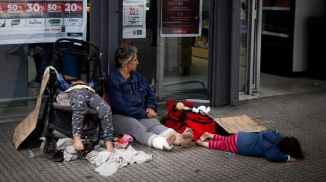 Uma mulher com dois filhos pedindo esmola em frente a um supermercado em Buenos Aires.