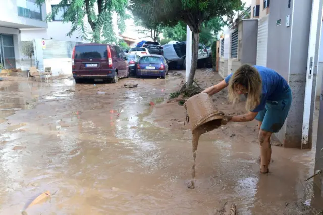 Mulher branca usa balde para tirar lama de sua casa