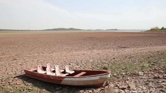 Um barco com seis assentos num leito de rio seco, com o chão de terra rachado pela falta de água