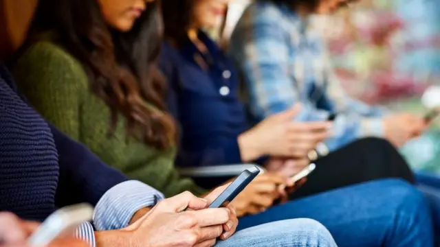 Mulheres sentadas lado a lado, segurando celulares