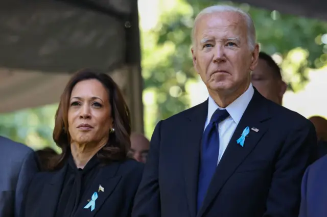 Kamala Harris ve Joe Biden, siyah ceketleri var, mavi kurdela takmışlar, uzağa bakıyorlar