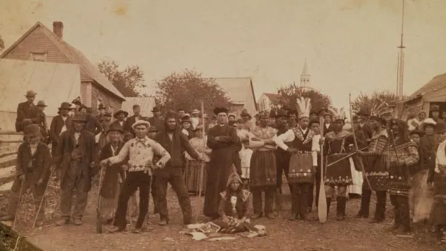 Um religioso e colonos russos posam para a foto junto a nativos vestidos com trajes tradicionais na cidade de Sitka, no Alasca, em torno de 1900