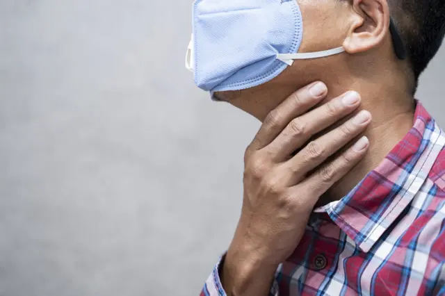 Homem usando máscara facial e colocando a mão na garganta