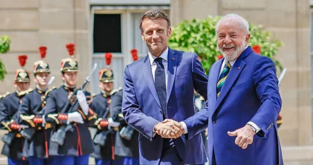 Lula e Macron apertando mãos com guardas da república francesa ao fundo em cerimônia oficial