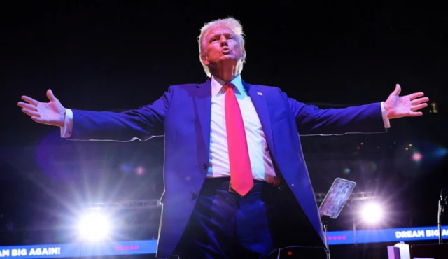 Trump abrindo os braços em arena iluminada durante grande evento