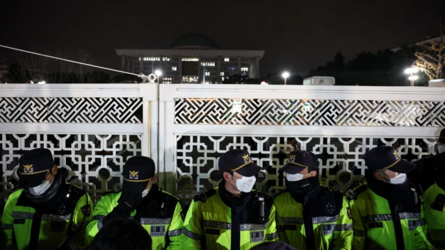 Des policiers portant des casquettes, des masques et des vestes à haute visibilité montent la garde devant la porte de l'Assemblée nationale après que le président de la Corée du Sud a déclaré la loi martiale.